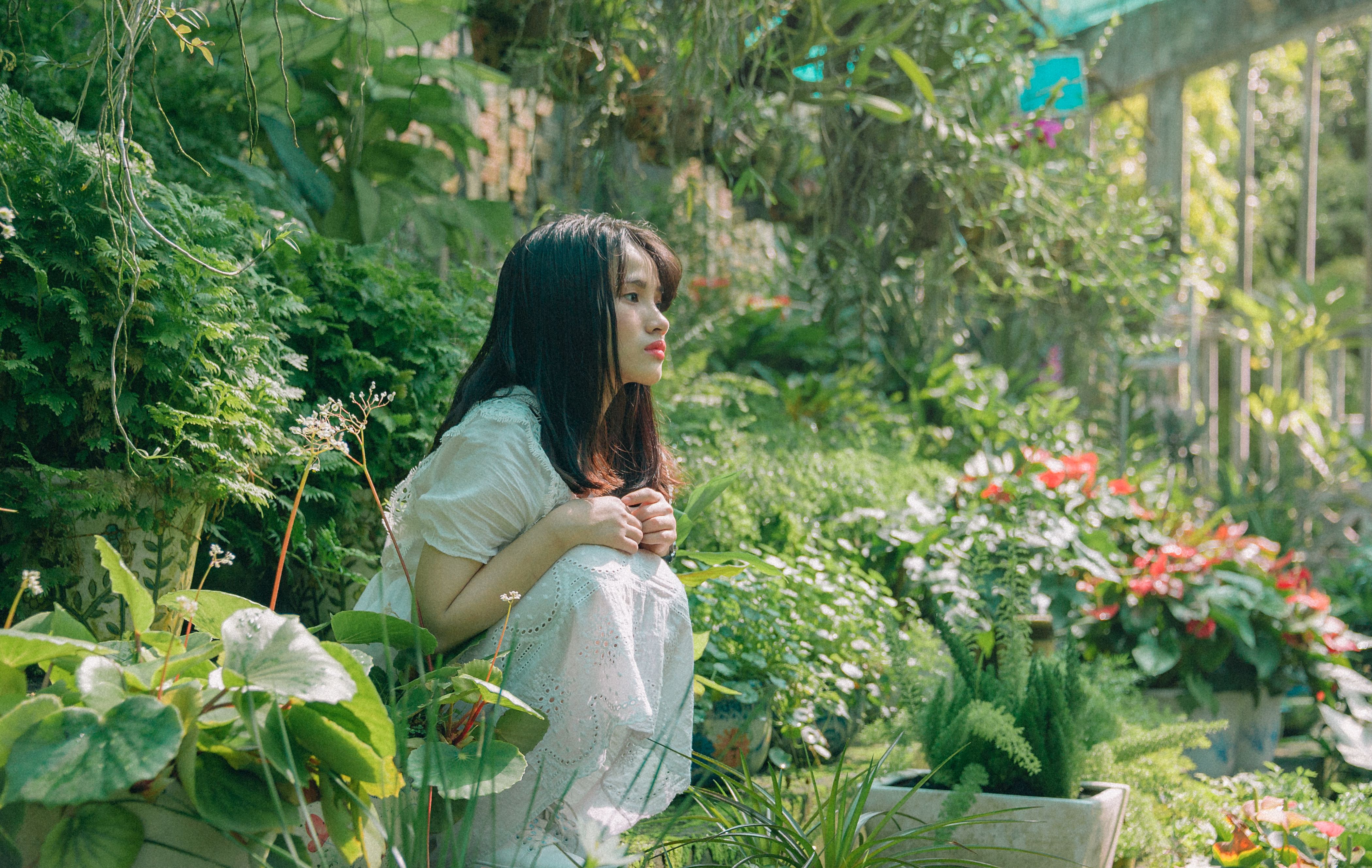 A woman enjoying a peaceful moment surrounded by greenery and flowers in a garden.