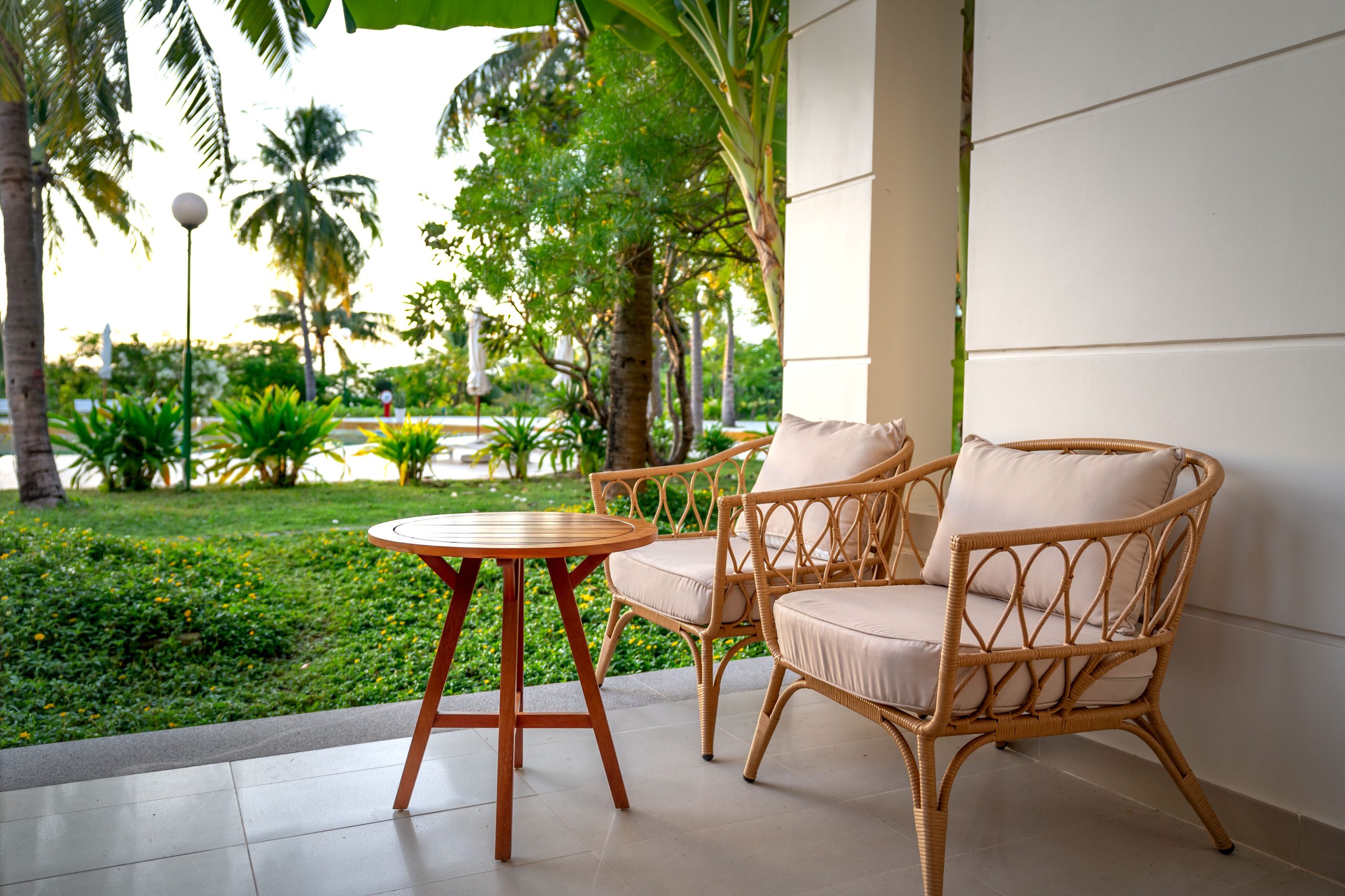 Rattan chairs on a serene patio overlooking a lush tropical garden, offering a comfortable place to relax outdoors.